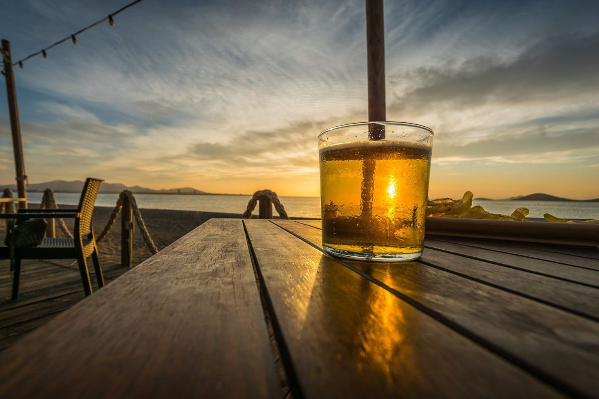 Glass of beer on a table by the beach during sunset