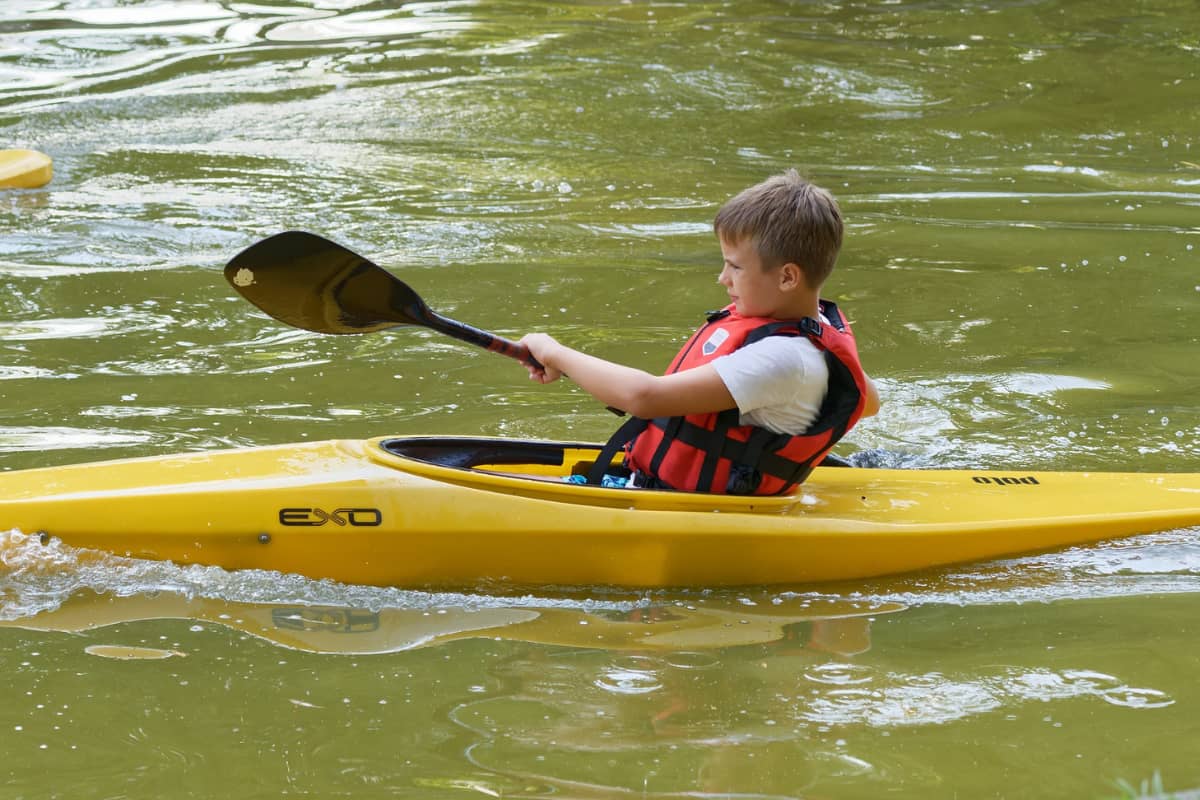 Boy riding a yellow sit-inside kayak and paddling by himself