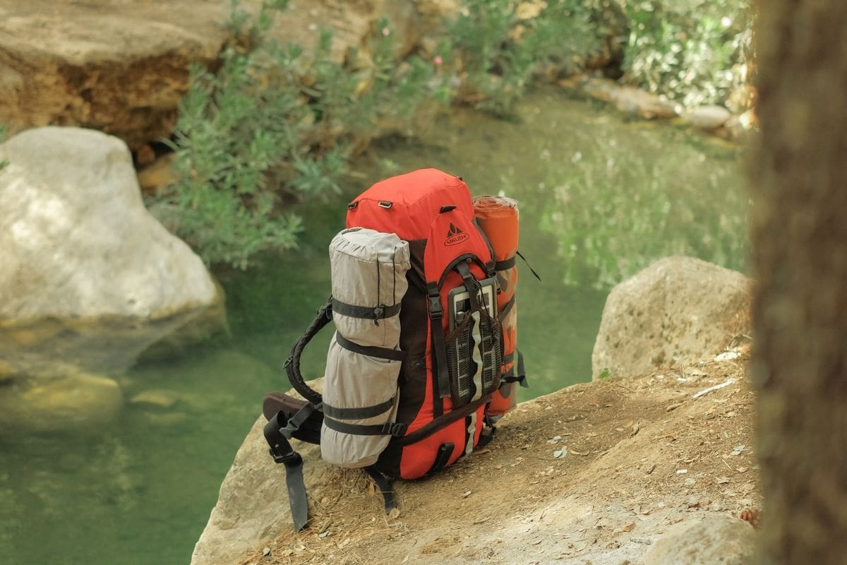 Backpack containing camping supplies on top of a rock beside a pond