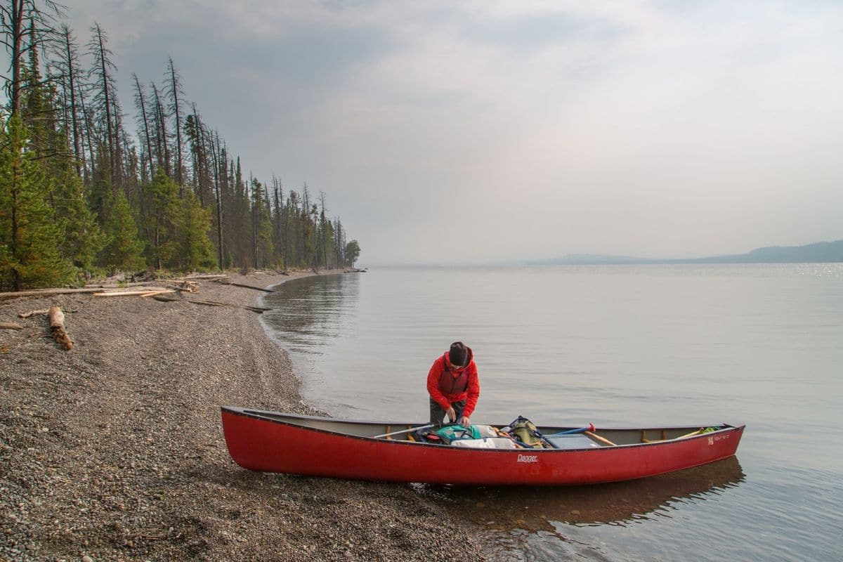 Person loading supplies and equipment onto a canoe by the lake shore