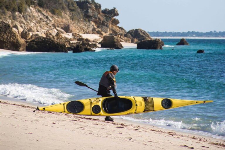 Person carrying a kayak alone by the shore near the water