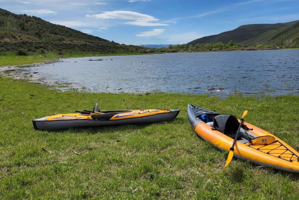 Two inflatable kayaks on the grass near a lake