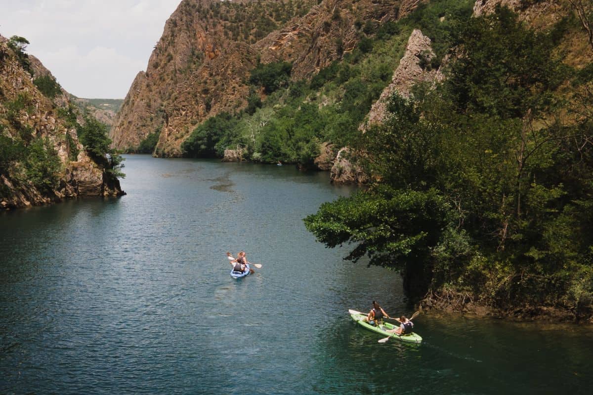 People riding on two kayaks along a river between two mountains