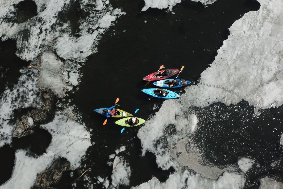 Aerial view of five people riding kayaks in a lake with icy waters