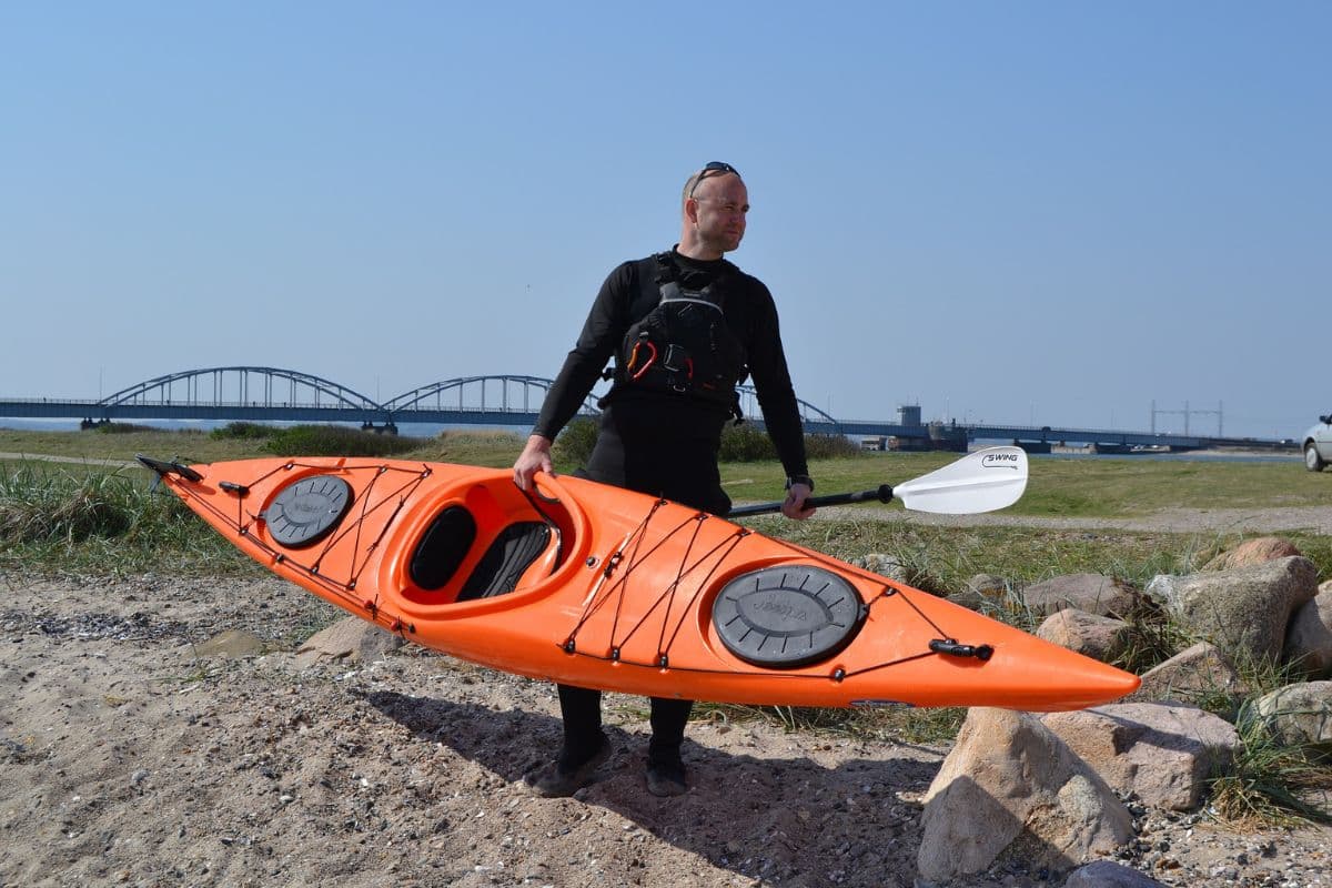 Man lifting up an orange kayak alone while holding a paddle
