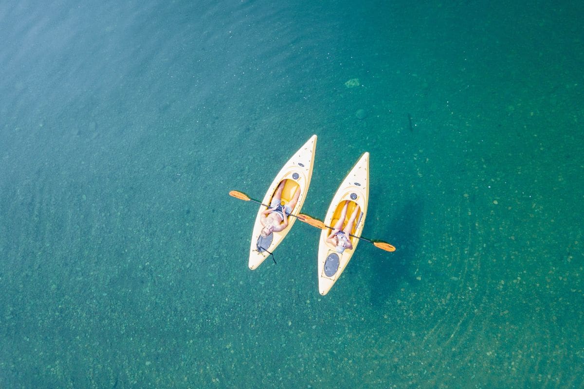 Bird's eye view of two people relaxing on kayaks in calm, shallow waters