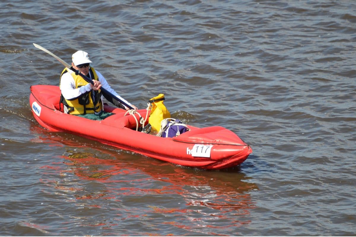 Man riding a red inflatable tandem kayak with equipment at the front seat