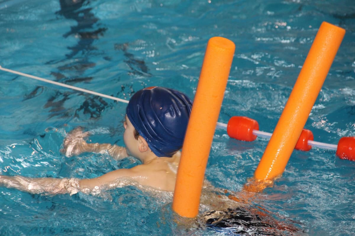 Boy swimming in a pool using a pool noodle for support