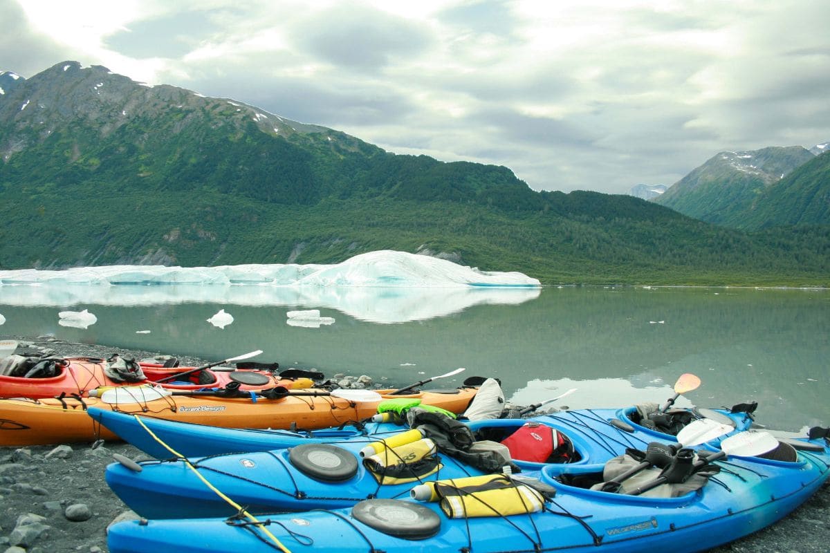 Multiple touring kayaks in front of an iceberg