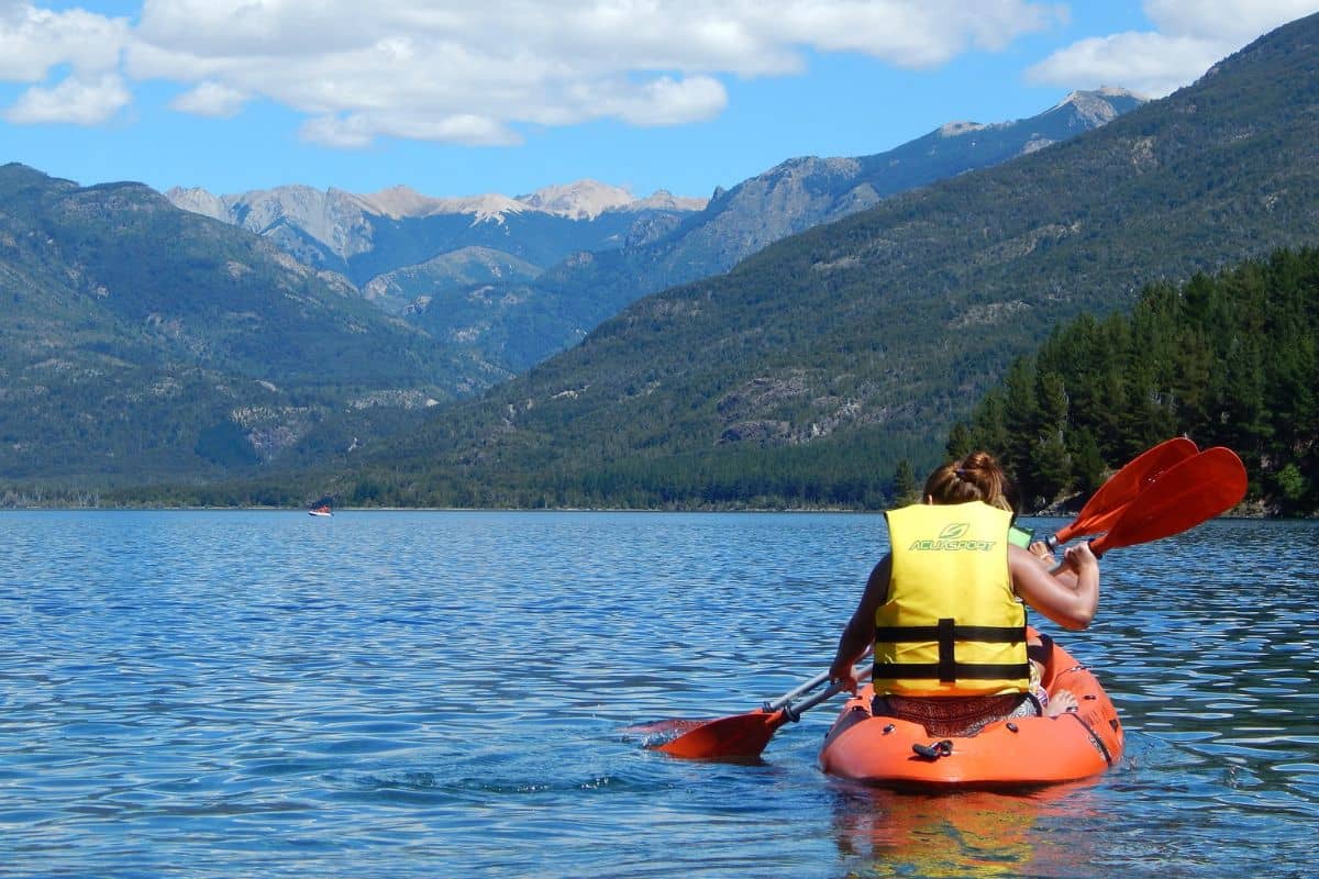 Woman riding a kayak wearing a personal flotation device or life jacket